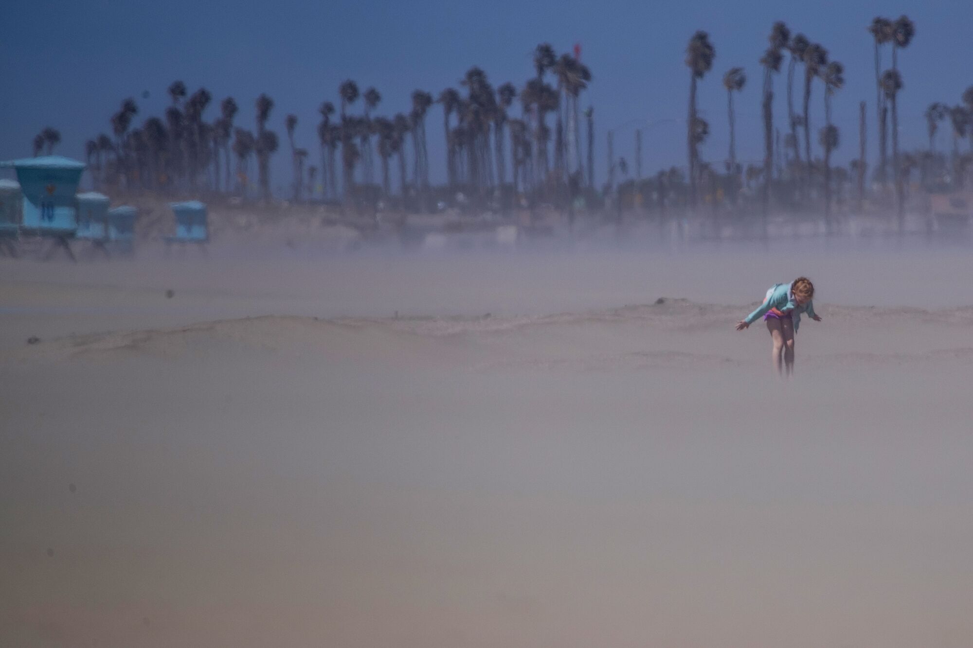 A child plays in the blowing sand and cold wind in Huntington Beach Wednesday.
