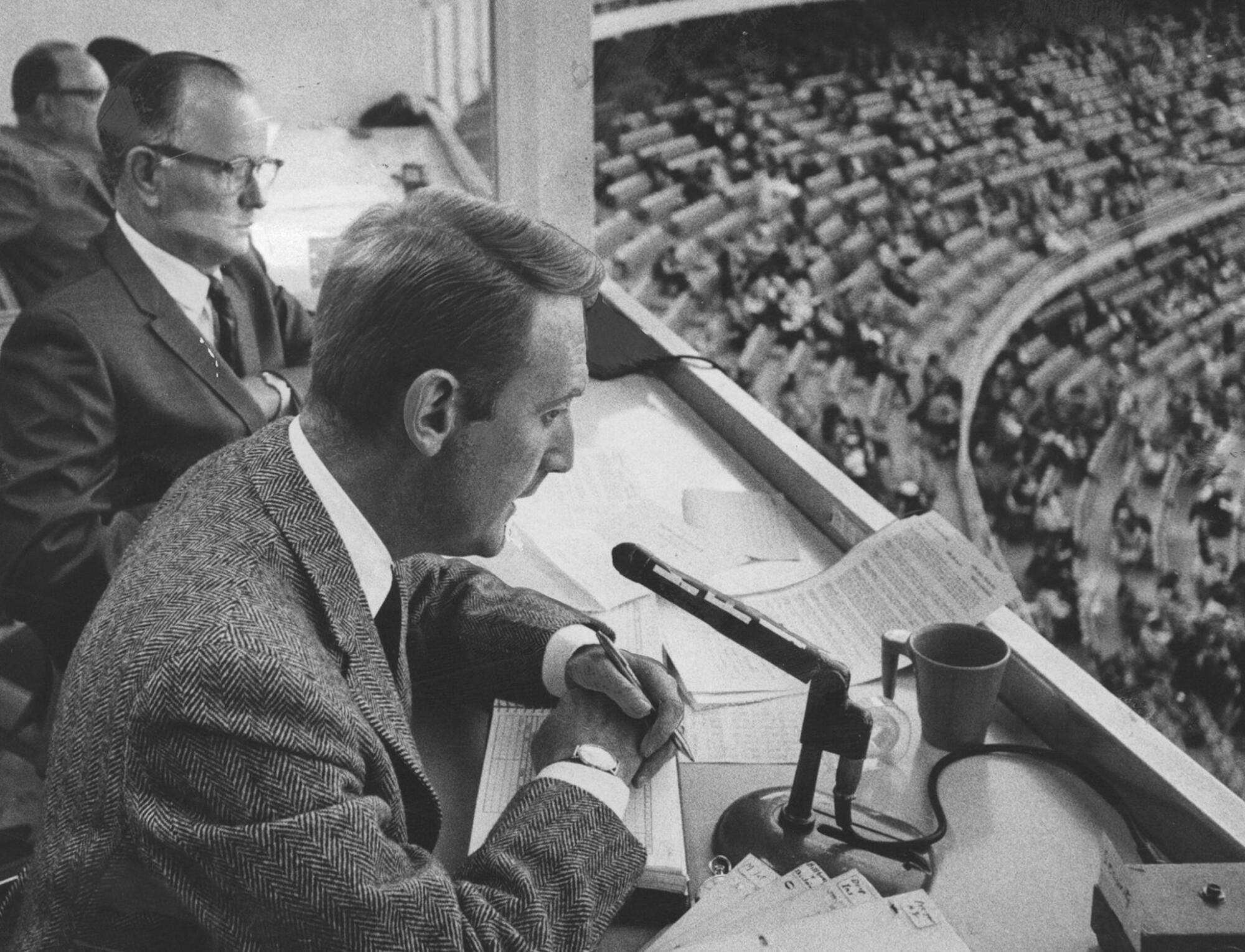 Vin Scully sits next to broadcast partner Jerry Doggett while calling a game at Dodger Stadium in 1967.