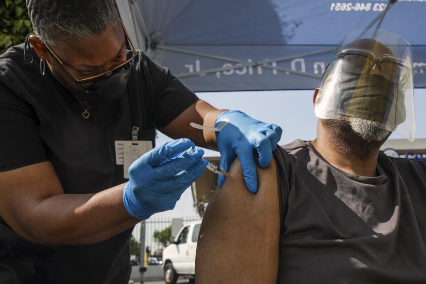 Los Angeles, CA - July 16: Eon Walk, left, administers a Pfizer-BioNTech vaccine to Daryl Black at a mobile COVID-19 vaccine clinic, hosted by Mothers In Action in collaboration with L.A. County Department of Public Health at Mothers in Action on Friday, July 16, 2021 in Los Angeles, CA. (Irfan Khan / Los Angeles Times)