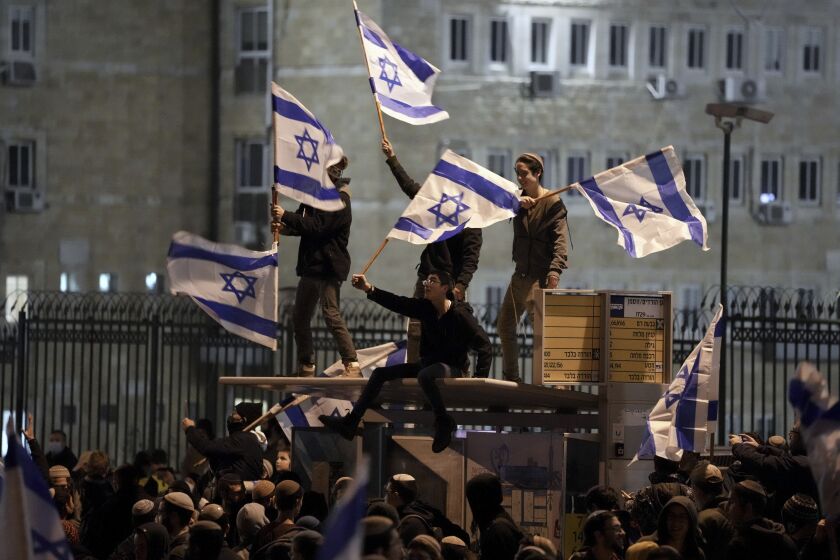 Israeli nationalists weave flags during a protest outside the parliament building in Jerusalem, calling on the government not to demolish a West Bank settlement outpost, Thursday, Jan. 13, 2022. (AP Photo/Ariel Schalit)