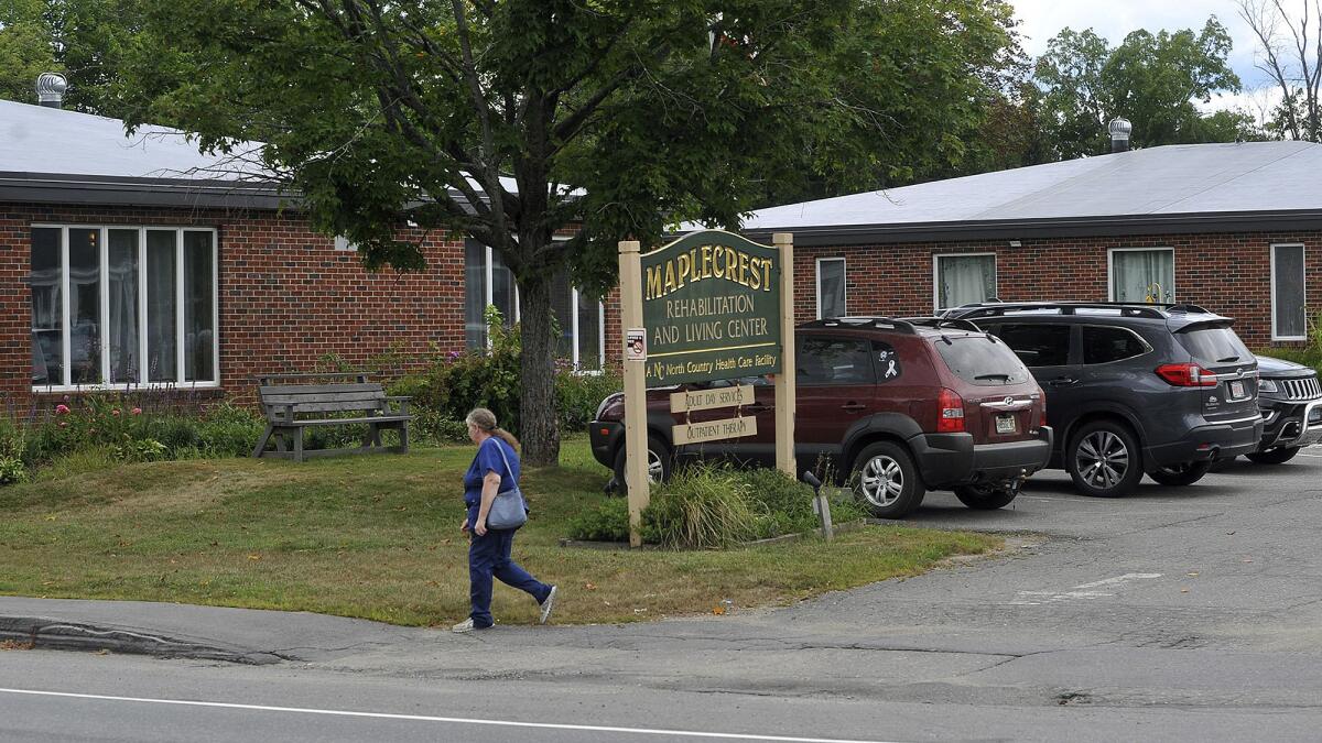 A woman walks past the parking lot and sign for Maplecrest Rehabilitation and Living Center.