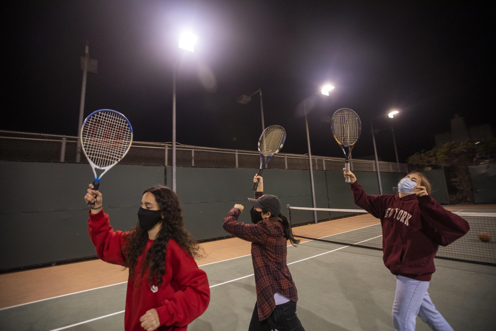 Alya Mehrtash, from left, Maryann Han and Sara Schwartz hold up tennis rackets while practicing a dance on a tennis court 