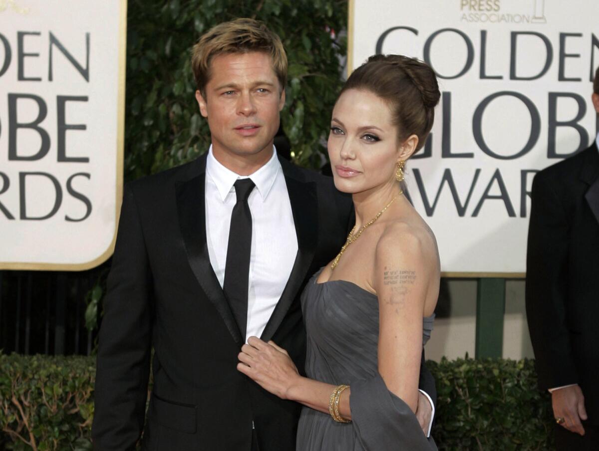Brad Pitt wearing a suit and Angelina Jolie wearing a strapless formal gown arrive on an awards show red carpet.