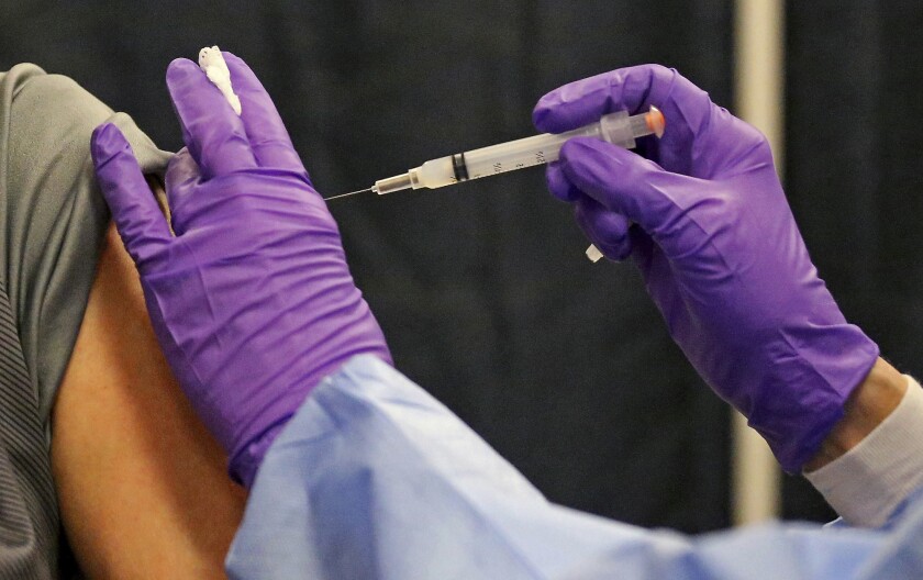 A gloved healthcare worker administers a vaccine.