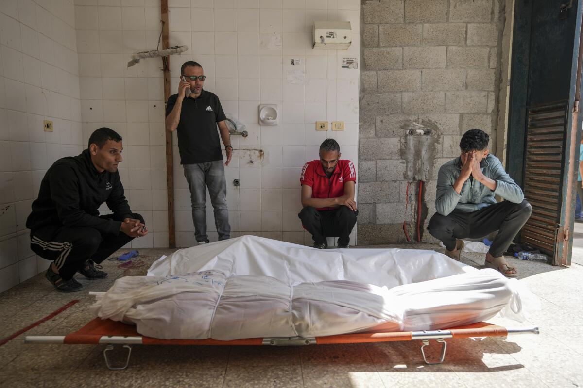 Palestinians mourn next to bodies on stretchers and covered in white plastic. 