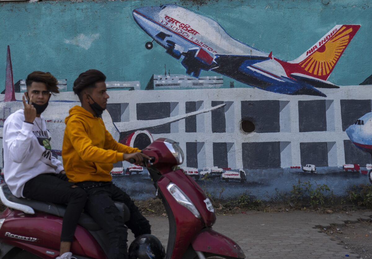 FILE - A scooterist drives past a wall painted with Air India planes in Mumbai, India, Thursday, Jan. 27, 2022. India's oldest and largest conglomerate Tata Sons will merge its Air India with Vistara, which it jointly runs with Singapore Airlines, according to a statement released on Tuesday. (AP Photo/Rafiq Maqbool, File)