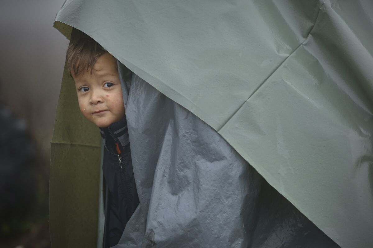 A migrant child peers from a makeshift tent at a camp housing migrants mostly from Afghanistan in Velika Kladusa, Bosnia, Tuesday, Oct. 12, 2021. Hundreds of migrants _ including small children, babies and elderly people _ have set up a new improvised camp in northwest Bosnia, determined to brave worsening weather and tough Croatian border police for a chance to reach Western Europe.(AP Photo)