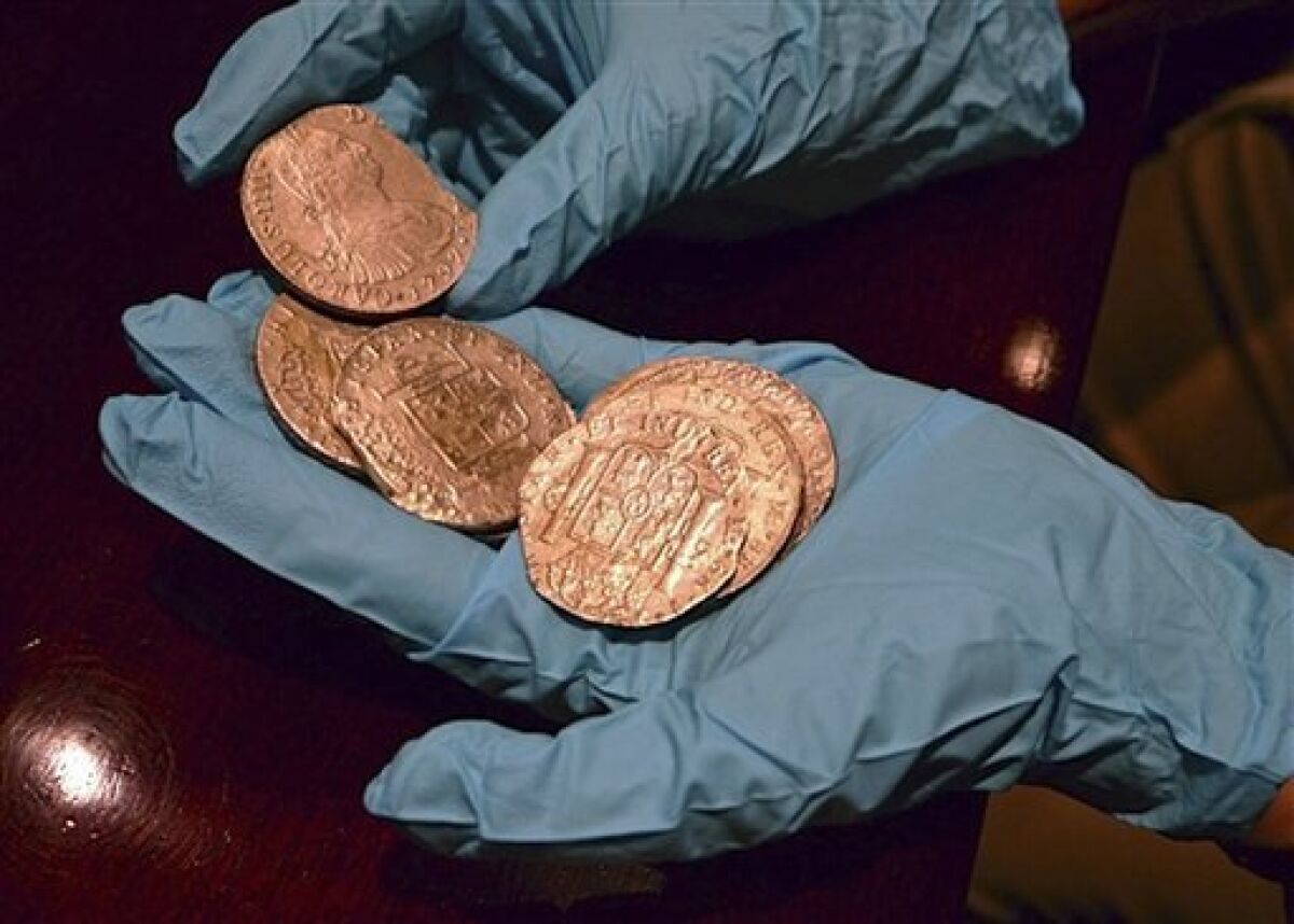 In this undated photo made available by the Spain's Culture Ministry, a member of the Ministry technical crew displays some of the 594,000 coins and other artifacts found in the Nuestra Senora de las Mercedes, a Spanish galleon sunk by British warships in the Atlantic while sailing back from South America in 1804, in a warehouse in Tampa, Fla. A 17-ton trove of silver coins recovered from the Spanish galleon was set to be flown Friday Feb. 24, 2012 from the United States to Spain, concluding a nearly five-year legal struggle with Odyssey Marine Exploration, the Florida deep-sea explorers who found and recovered it. (AP Photo/Spain's Culture Ministry)