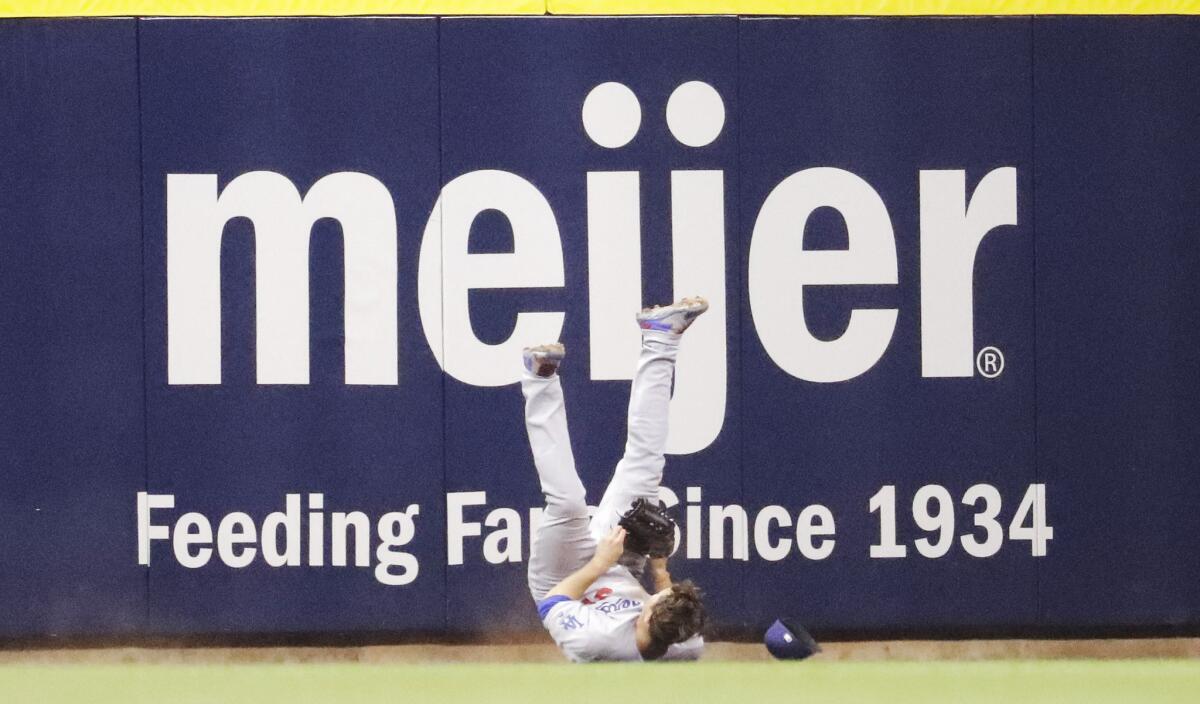 Dodgers center fielder Joc Pederson rolls on the ground after catching a ball and crashing into the wall during the eighth inning of a game against the Brewers.