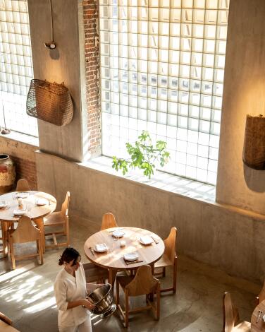 A server walks past tables under a large gridded window in the dining room of Yess restaurant in the Arts District.