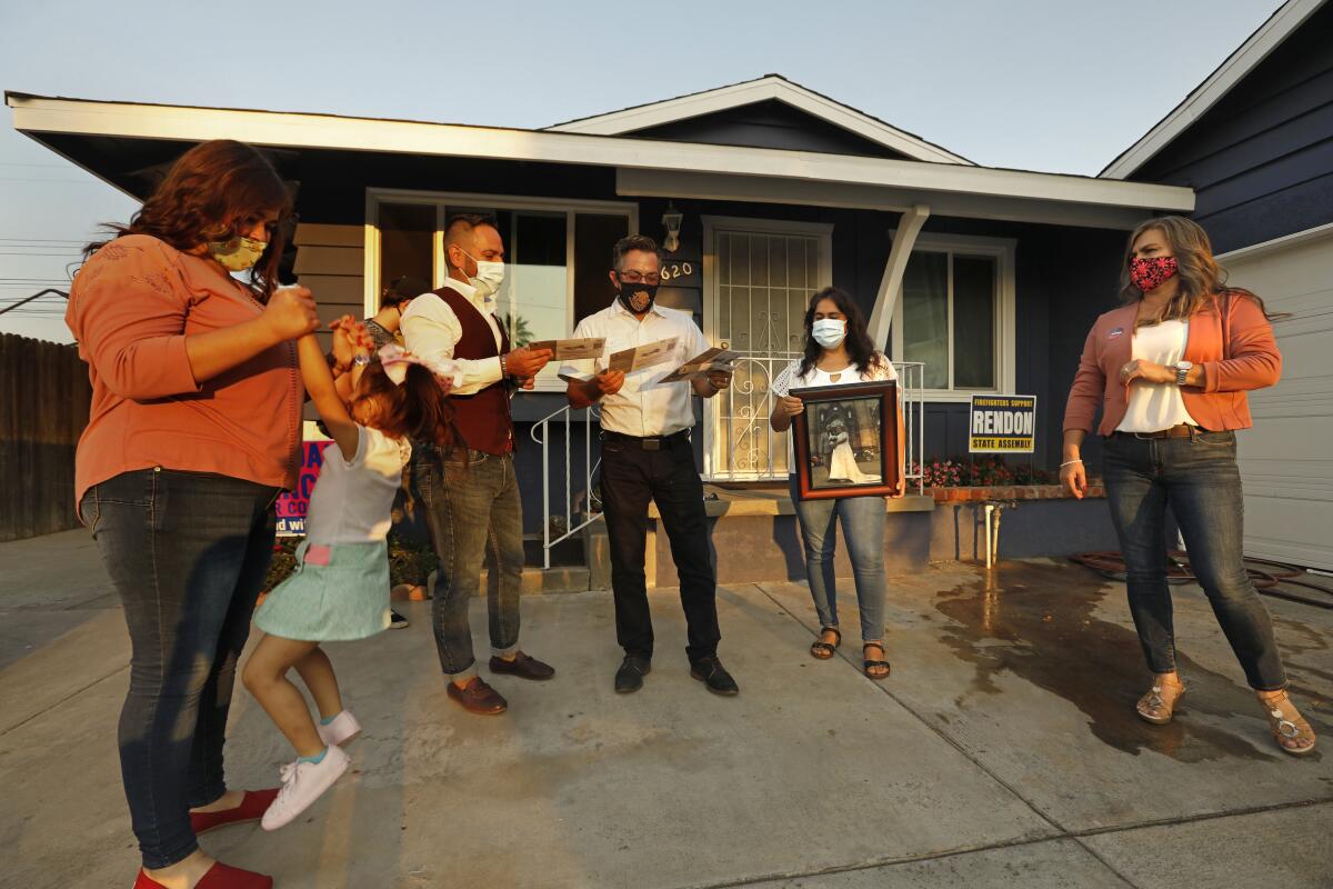 A family, all wearing face masks, stand in front of their house