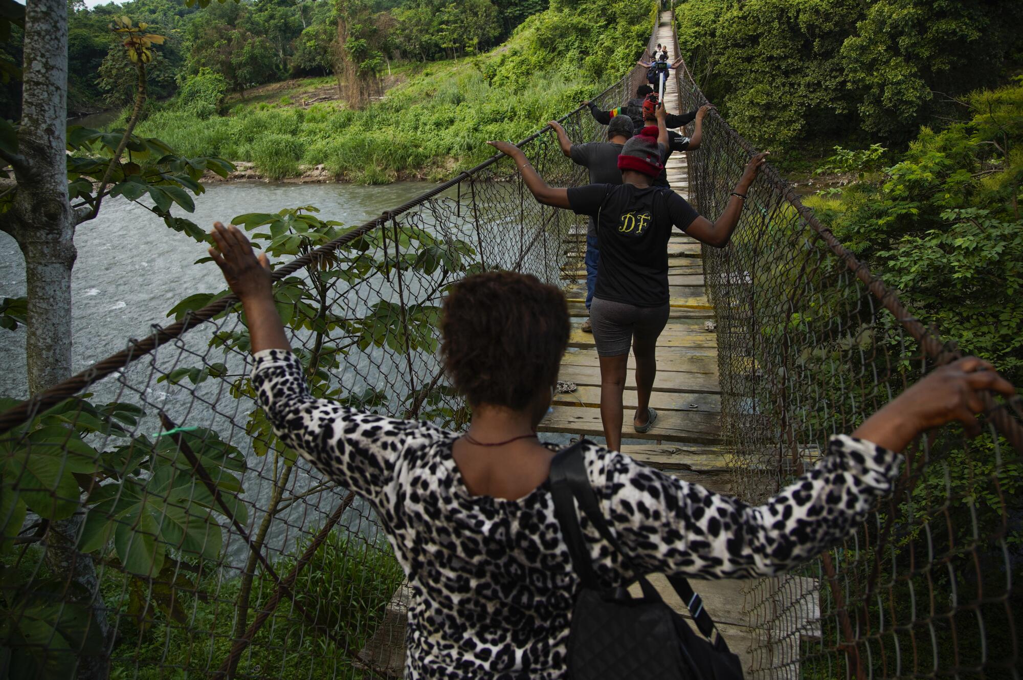 A group of Haitian migrants grip the sides of a bridge as they cross the Cahoacán river