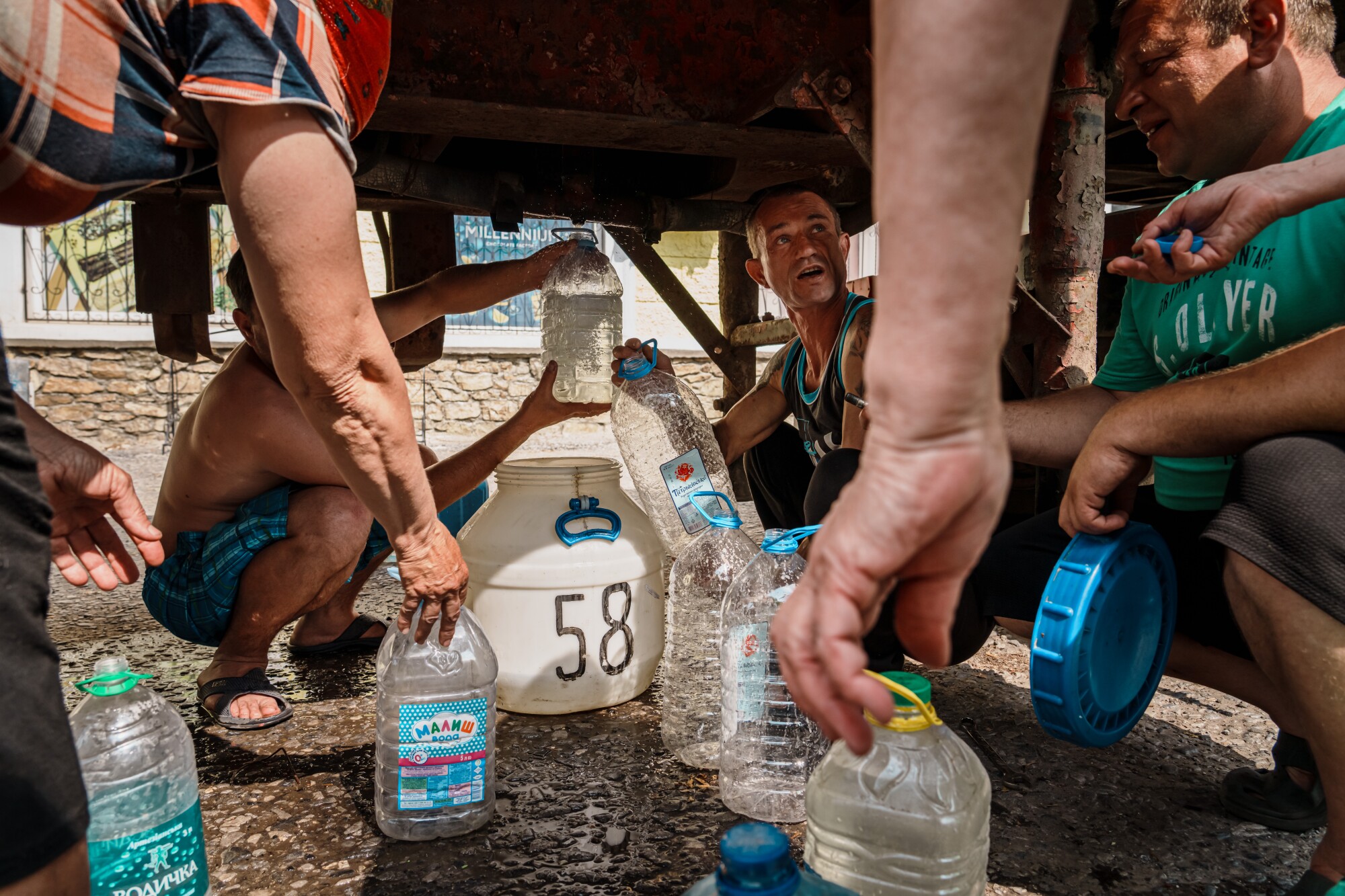 Residents go under the belly of a water truck to fetch water in Siversk, Ukraine.