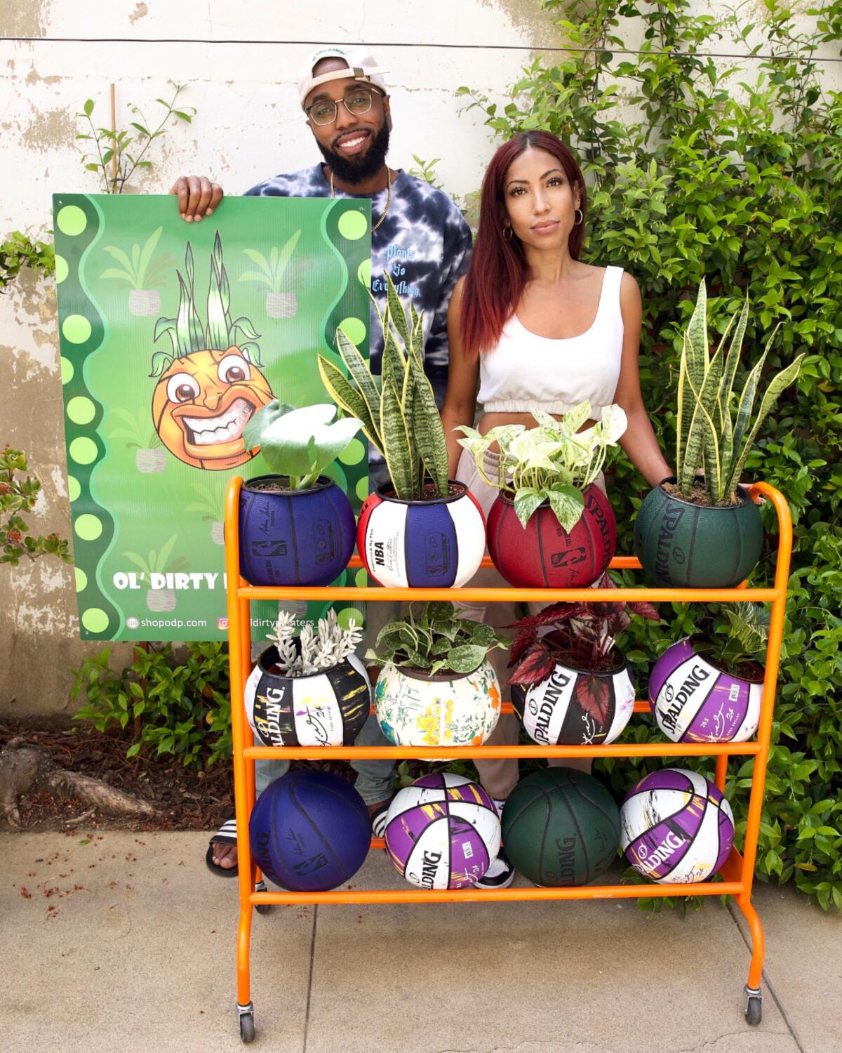 A man and a woman stand behind a rack of a basketballs-turned-planters.