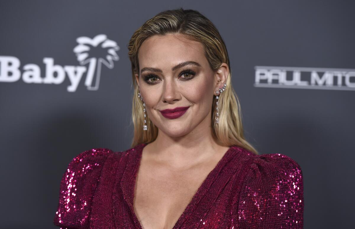 Hilary Duff wears a sparkly red dress as she poses for photos at a red carpet event.