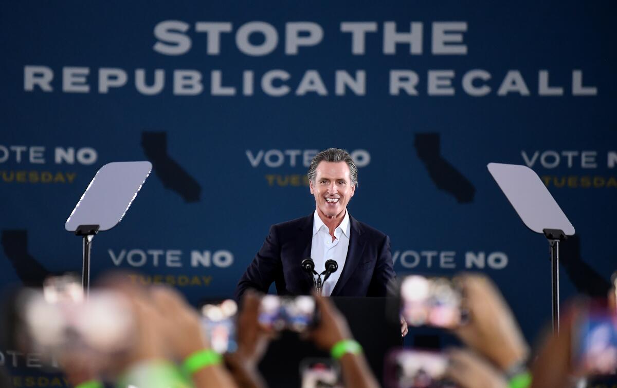 California Gov. Gavin Newsom smiles onstage at a rally against a backdrop reading "Stop the Republican recall" 
