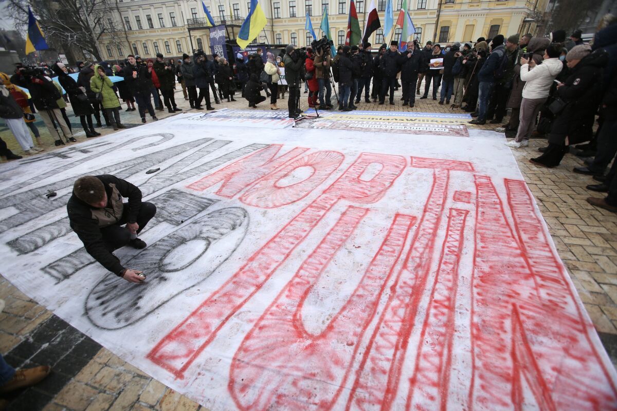 A man draws on a big poster on the ground with the words in black and red, "#Say no to Putin" 