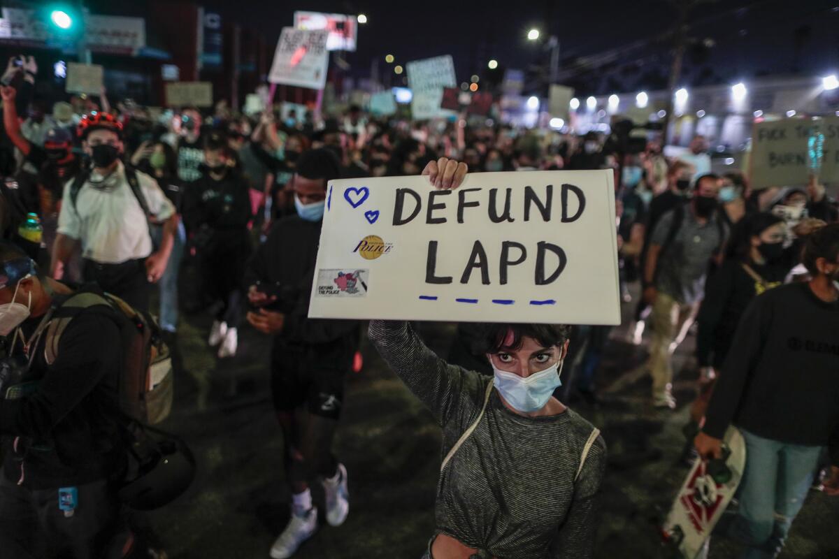 In a crowd, a protester holds up a "Defund LAPD" sign. 