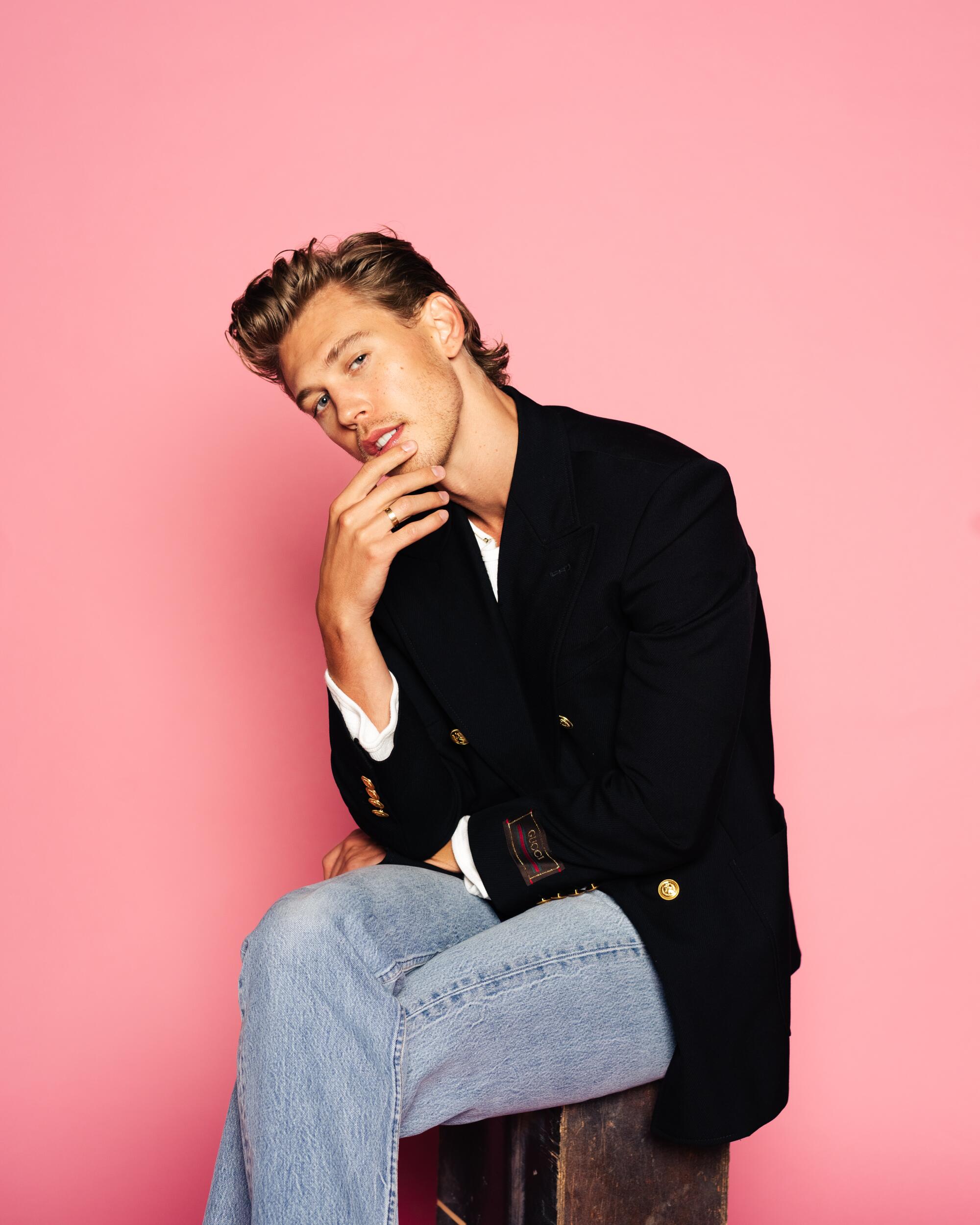 A man with blond hair poses for a portrait against a pink backdrop.