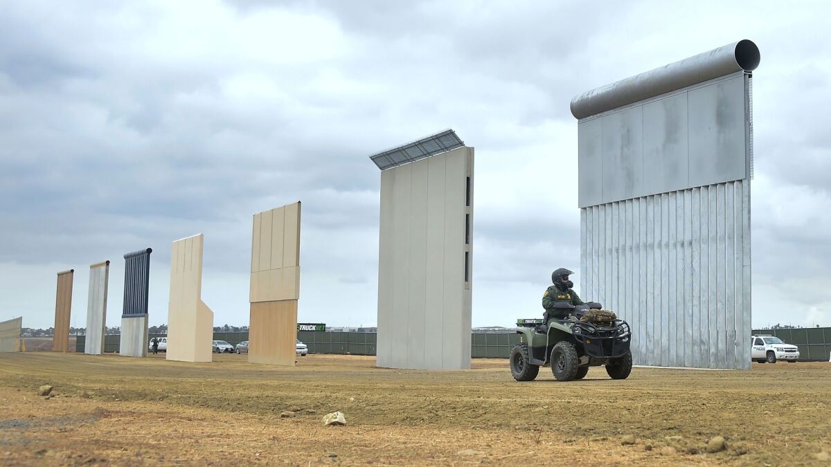 A border patrol officer rides past prototypes of President Trump's proposed border wall in San Diego.