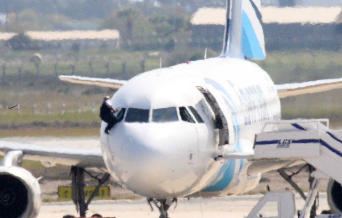 A person believed to be a member of the crew climbs out of a cockpit window of the hijacked EgyptAir A320 plane parked at a sealed off area of the Larnaca Airport, in Larnaca, Cyprus.