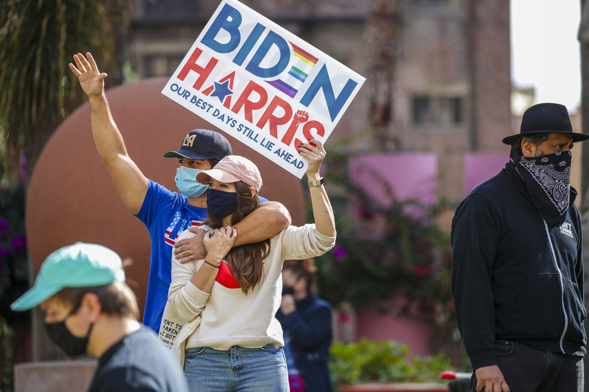 Two people hug and hold aloft a Biden-Harris sign