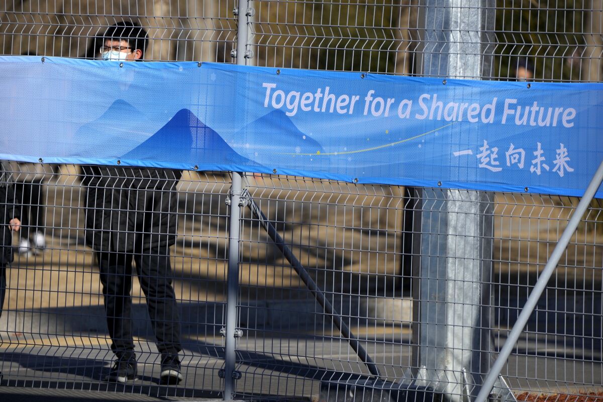 FILE - A person looks through the fence at the closed-loop area for Olympics personnel on the Olympic Green near at the 2022 Winter Olympics, Tuesday, Feb. 1, 2022, in Beijing. (AP Photo/Mark Schiefelbein, File)