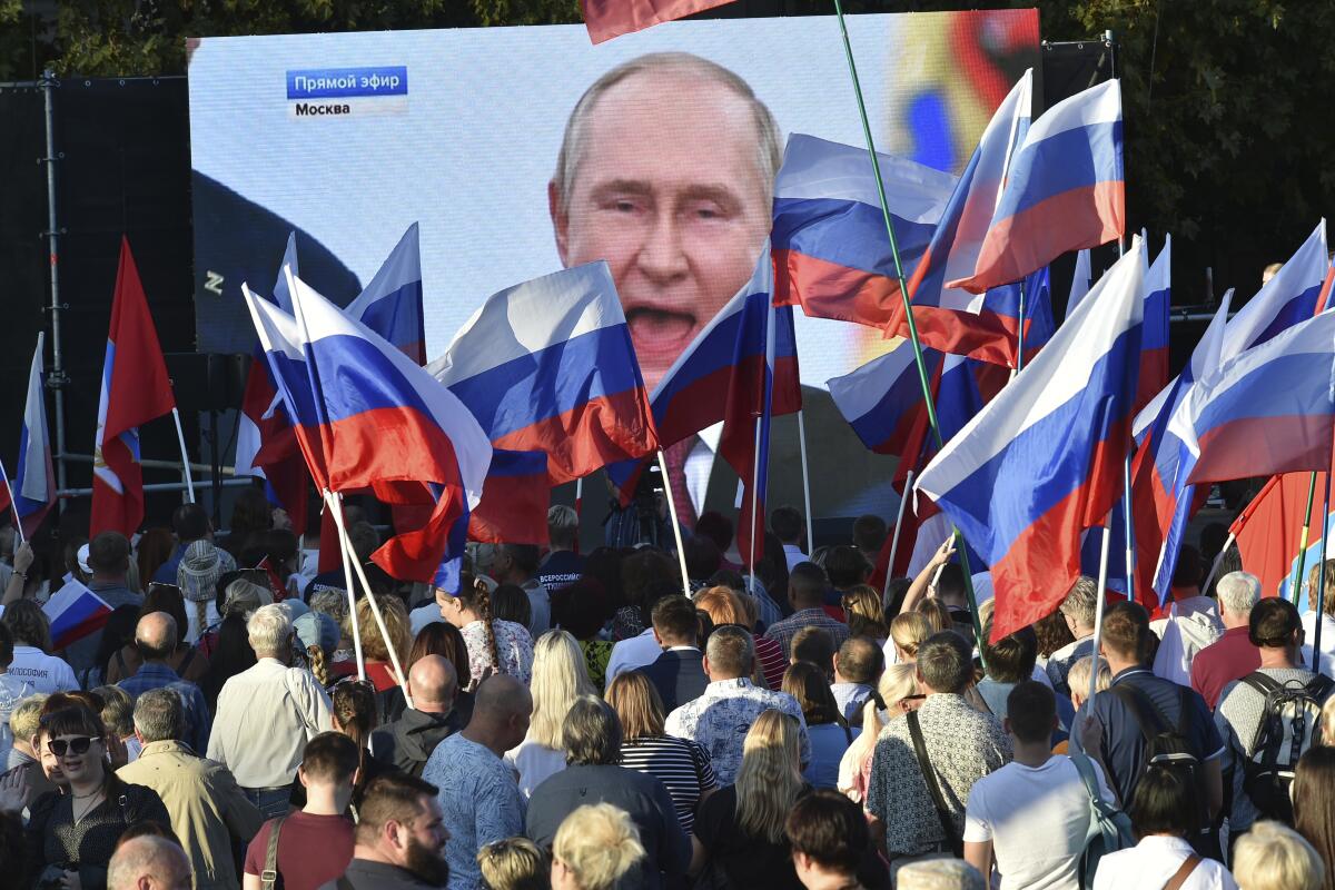 People watch Russian President Vladimir Putin speak on a large screen.