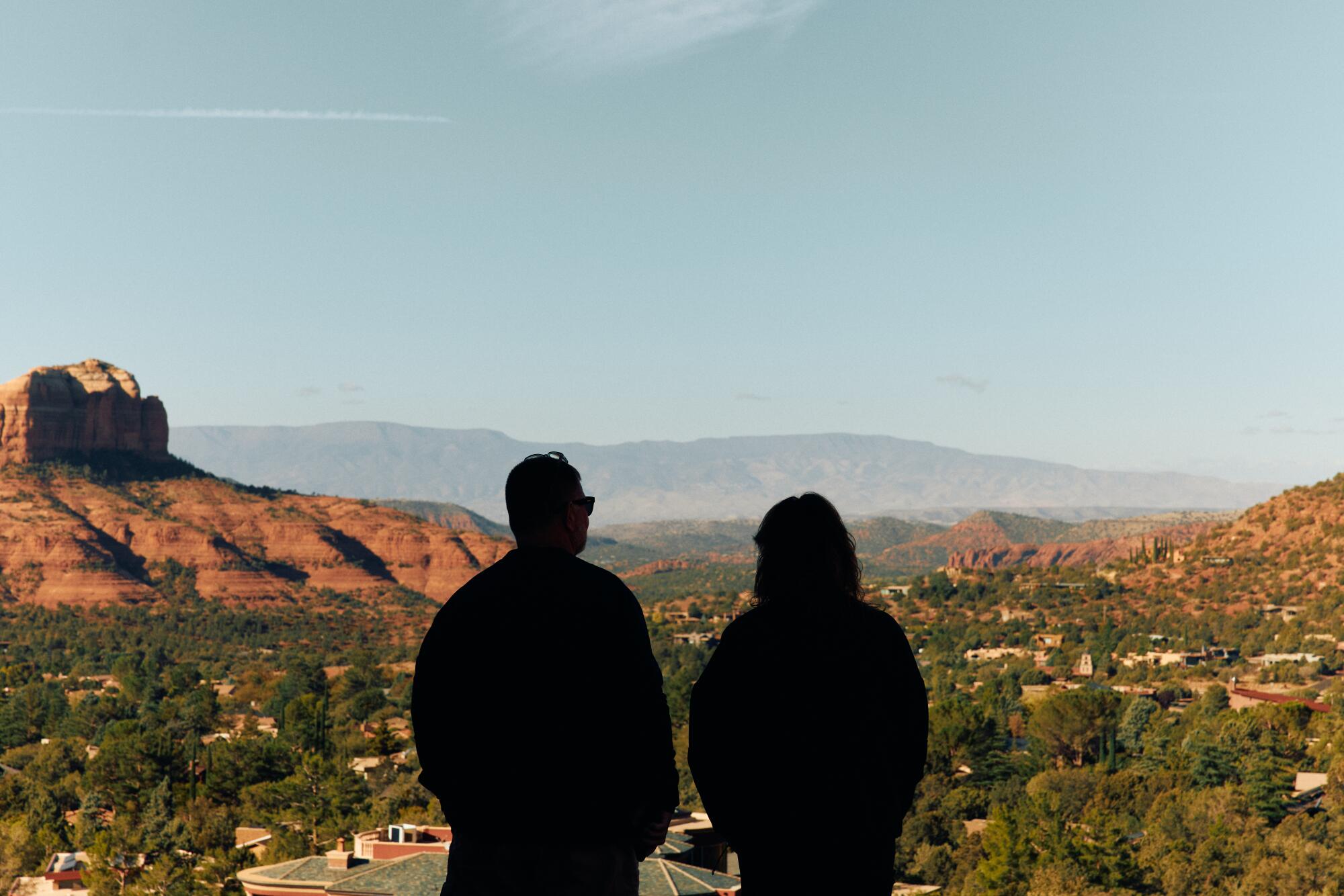 Two people look out at rock formations and trees at a Sedona viewpoint known as Chapel of the Holy Cross.