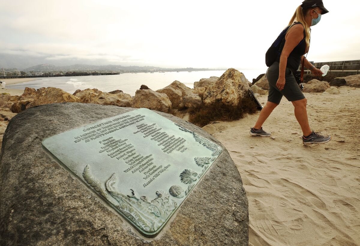 A woman walks on a beach past a boulder with a plaque on it