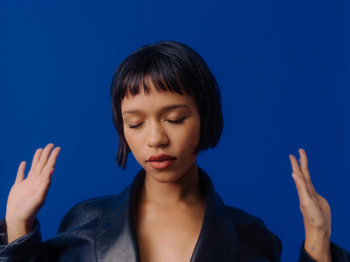 Taylor Russell closes her eyes and raises her hands for a portrait.