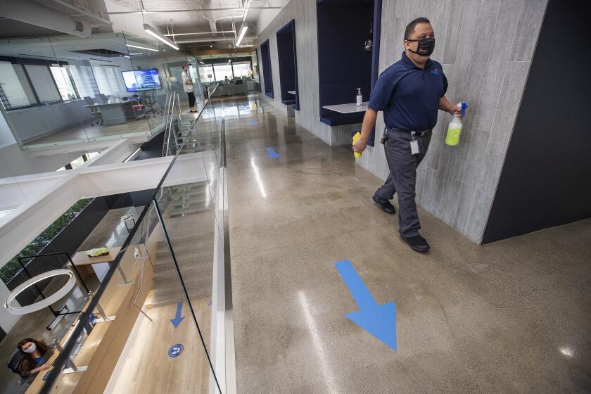 LOS ANGELES, CA - SEPTEMBER 17, 2020: Saul Mendoza, with building maintenance, walks with disinfectant while cleaning a common area at Hudson Pacific Properties, a big office landlord on Wilshire Blvd. in Los Angeles. Arrows taped on the floor are to maintain one way foot traffic to guard against the spread of the coronavirus. (Mel Melcon / Los Angeles Times)