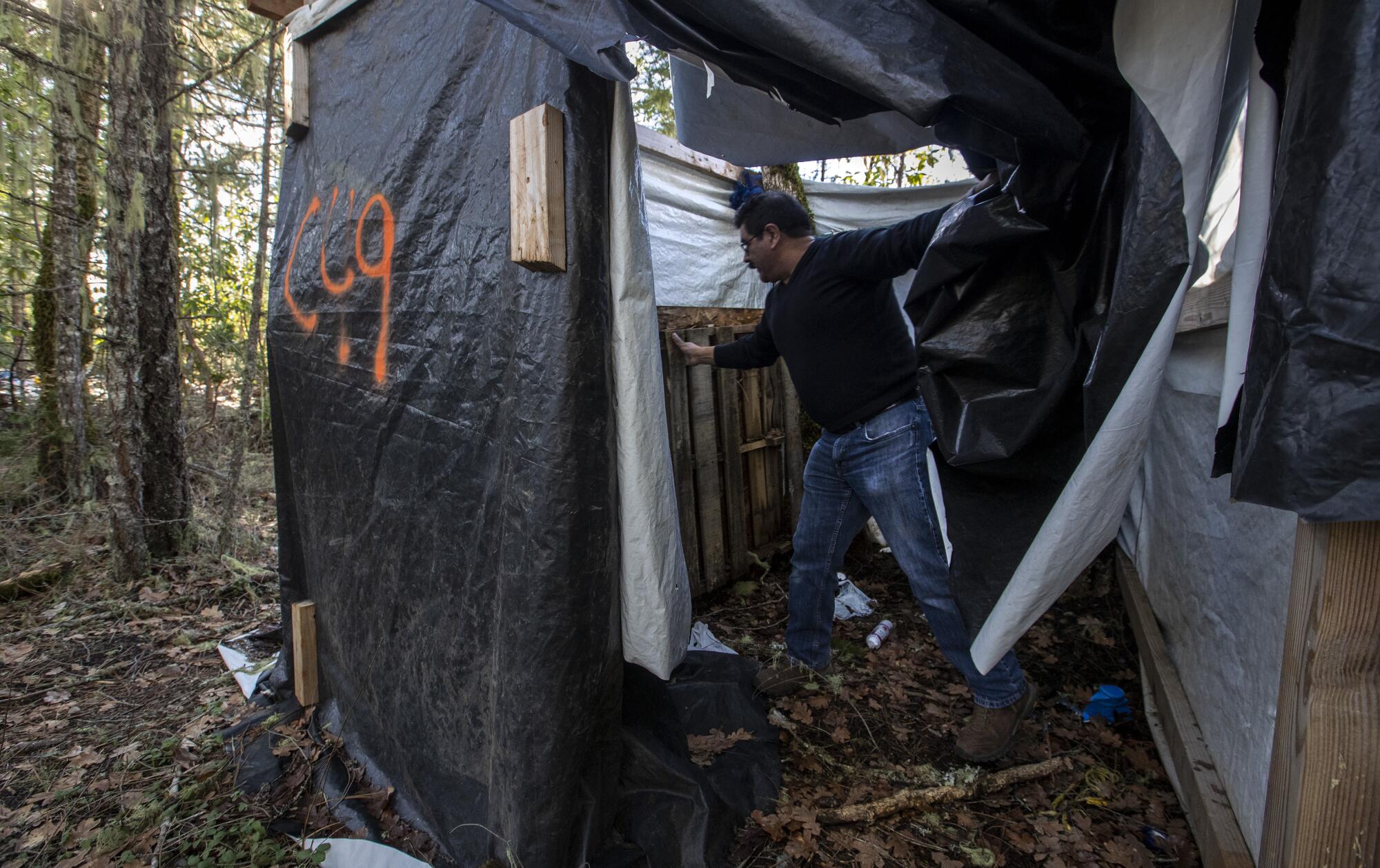 A man lifts a pallet inside a crude shower tent