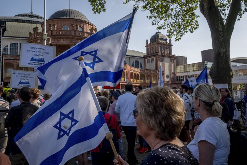 Women hold Israeli flags as they take part in a demonstration against a concert later the day of former Pink Floyd musician Roger Waters in the Festhalle, background, in Frankfurt, Germany, Sunday, May 28, 2023. The Festhalle was the the place where in the night of broken glasses 1938 about 3000 Jewish men where gathered to deport them to concentration camps. (AP Photo/Michael Probst)