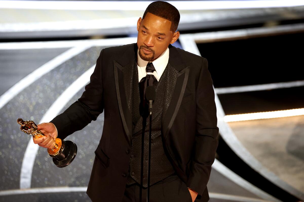 Will Smith stands onstage holding his Oscar award