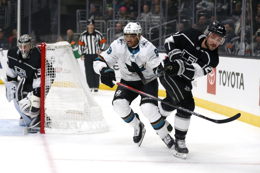 LOS ANGELES, CALIFORNIA - NOVEMBER 25: Alec Martinez #27 of the Los Angeles Kings passes the puck as Evander Kane #9 of the San Jose Sharks defends during the first period at Staples Center on November 25, 2019 in Los Angeles, California. (Photo by Katharine Lotze/Getty Images)