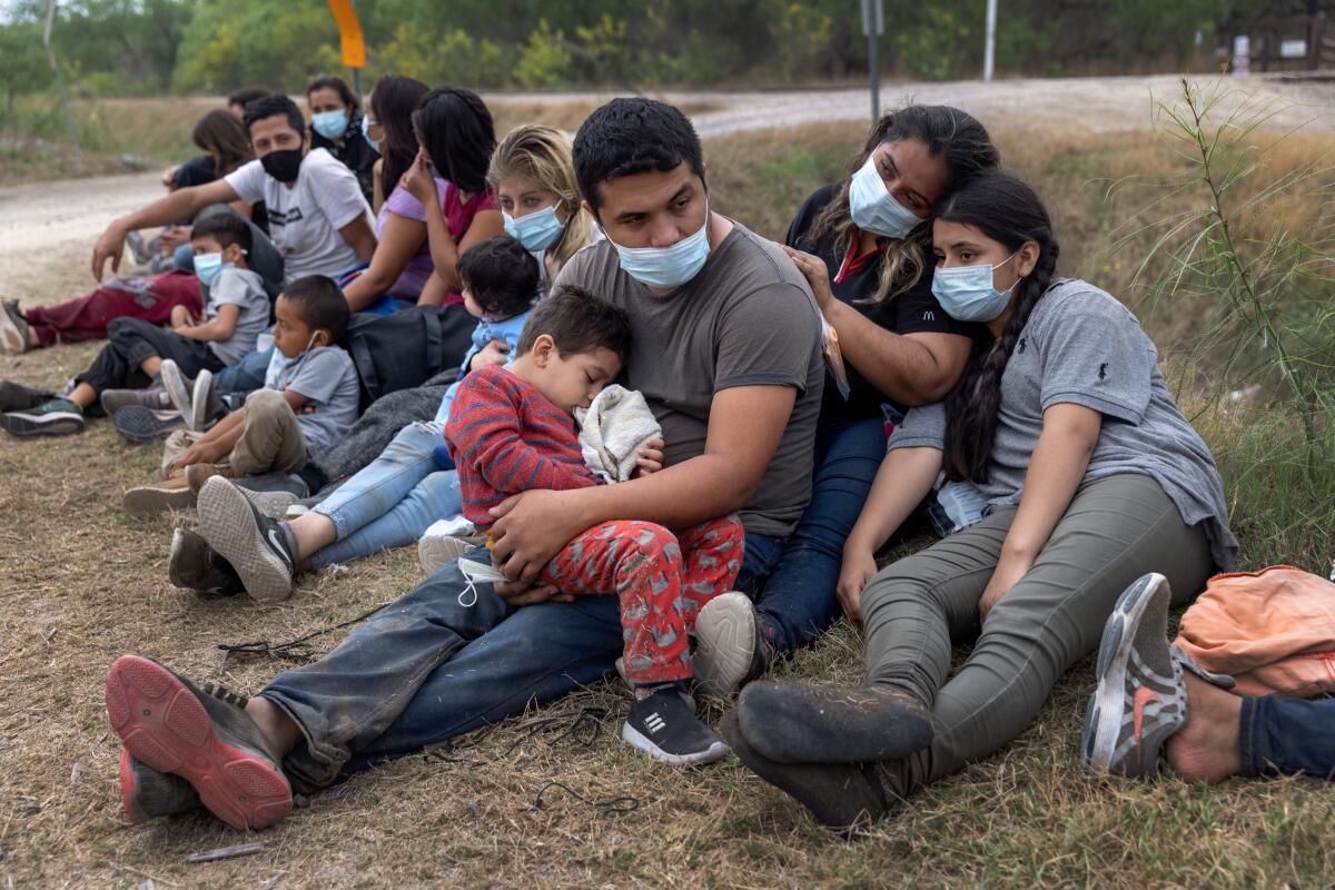 Families sit on the ground outside waiting