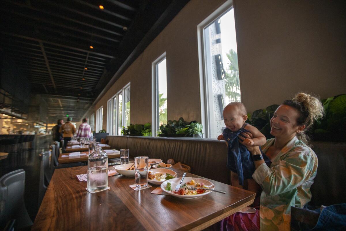 A mother holds her daughter at a restaurant booth.