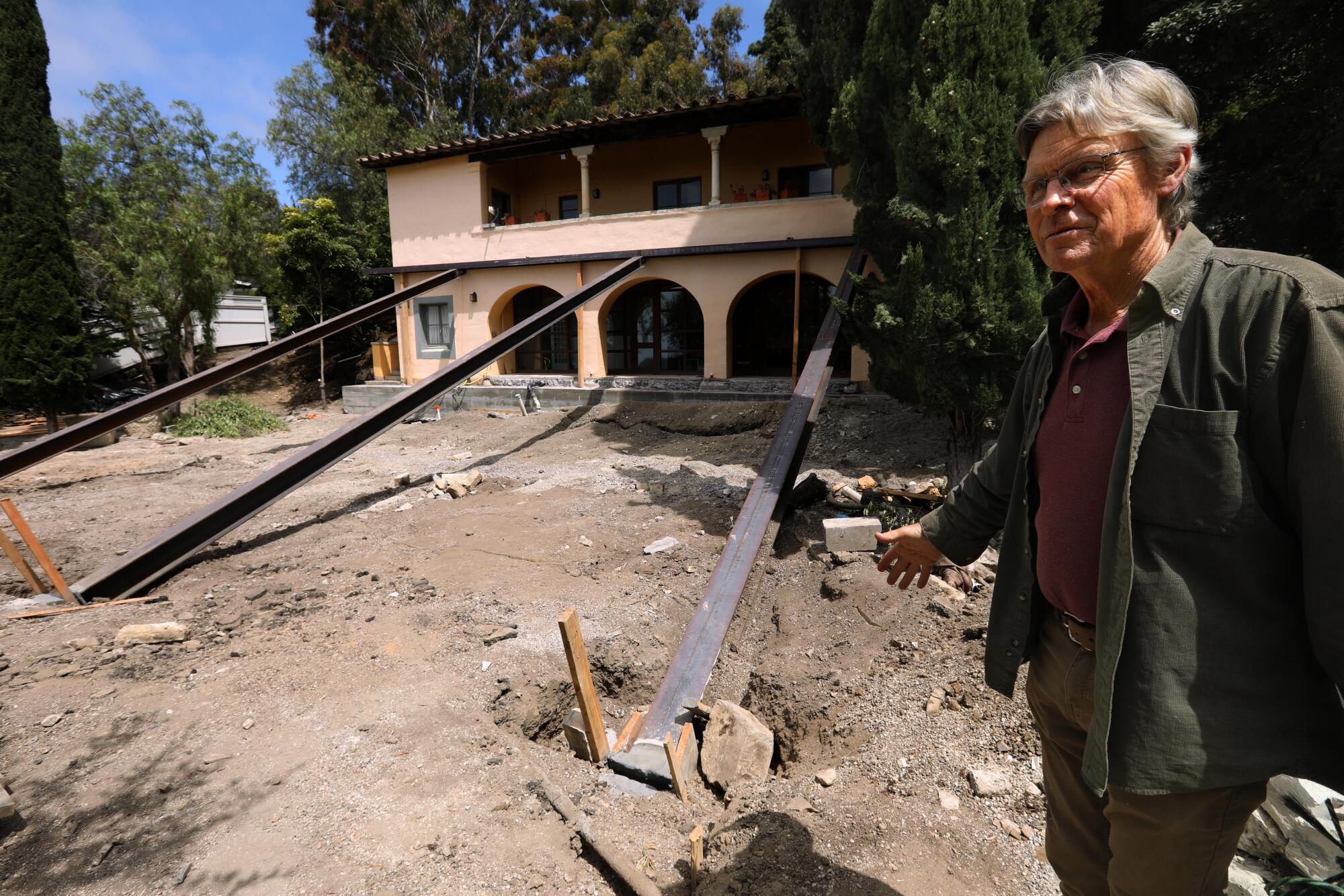 A man stands near a home supported by metal bars.