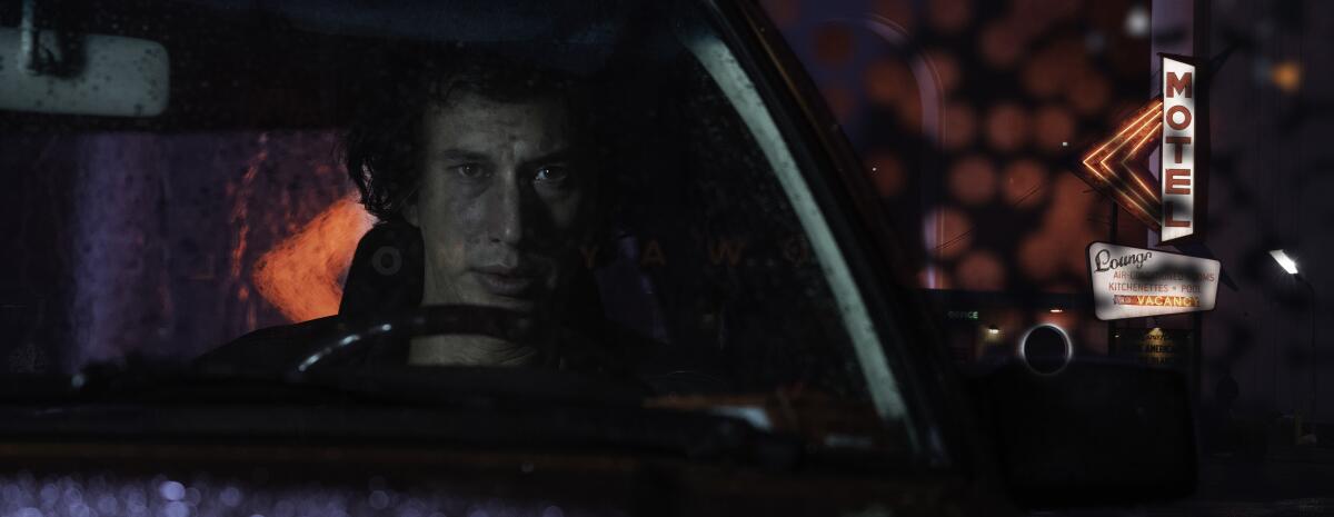Adam Driver in the driver seat of a car, with a motel sign in the background