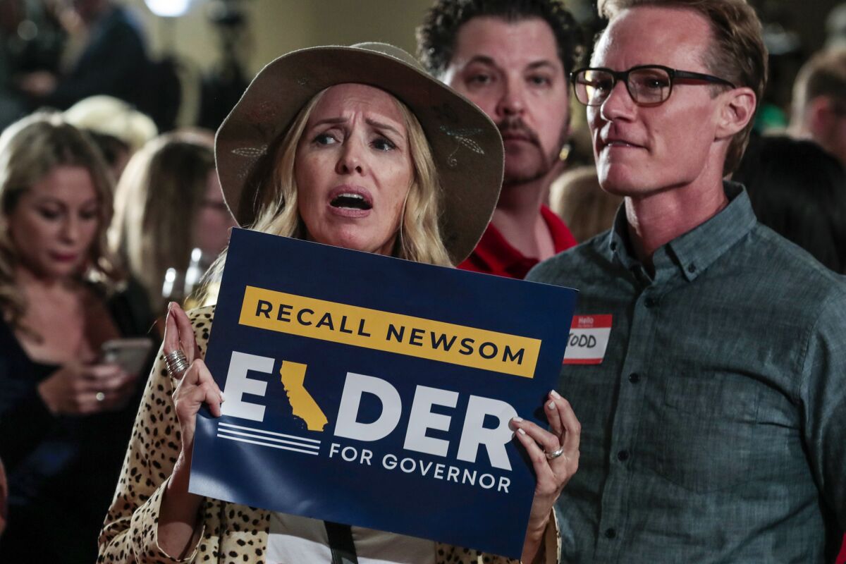 A woman holding a sign supporting Larry Elder crosses her fingers.