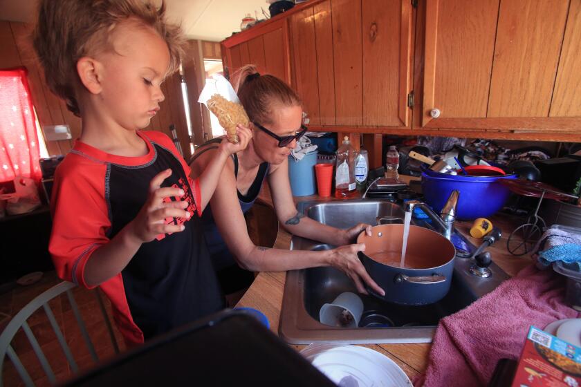 Edwards, CA - May 26: 5-year-old Adam Ezelle waits to help as his mother Dana Ezelle fill a pot with tap water in their kitchen to cook noddles for dinner prep on Friday afternoon. At Fountain Trailer Park in North Edwards, residents have been unable to safely drink or cook with the tap water for years, which is tainted with arsenic. Dana Ezelle and Adam, her 5-yr-old son, live here. They rely on bimonthly water deliveries provided by a nonprofit to cook and drink. But often that supply is not enough to last them until the next distribution, and Dana doesn't make enough money to buy her own bottled water, so they're forced to sometimes drink and cook with it. Friday, May 26, 2023 in Edwards, CA. (Alex Horvath / Los Angeles Times).