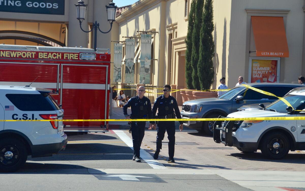Newport Beach police officers cross behind crime scene tape outside Fashion Island.