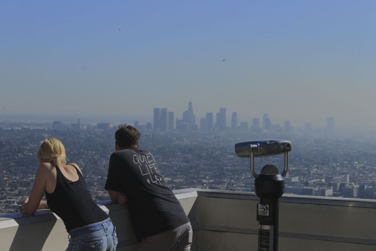 Visitors to the Griffith Observatory take in a smoggy view of the L.A. Basin. More than 7 million Californians live in highly polluted and socioeconomically vulnerable areas, which put them at higher risk for cancer, asthma, low-birth weights and other negative health effects, according to state research.