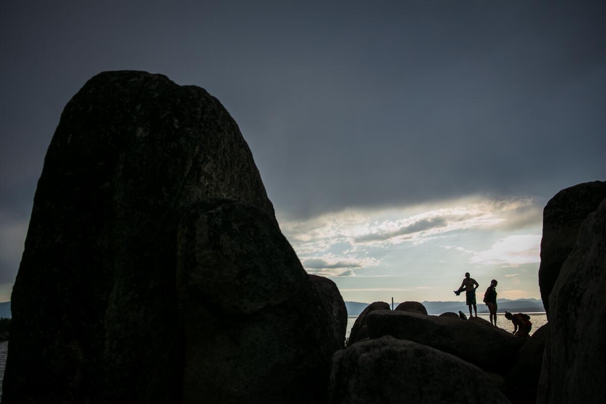Visitors silhouetted by glimmering sunlight climb rocks on the shore of Lake Tahoe