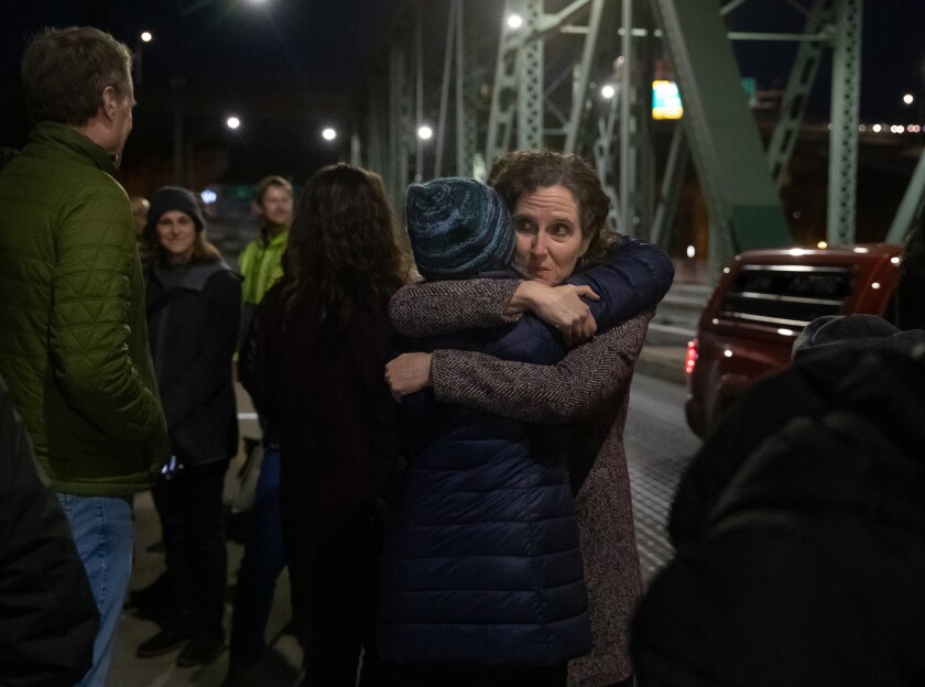 Jennifer Vines abraza a una amiga tras un momento de silencio al cumplirse el segundo aniversario de la pandemia 
