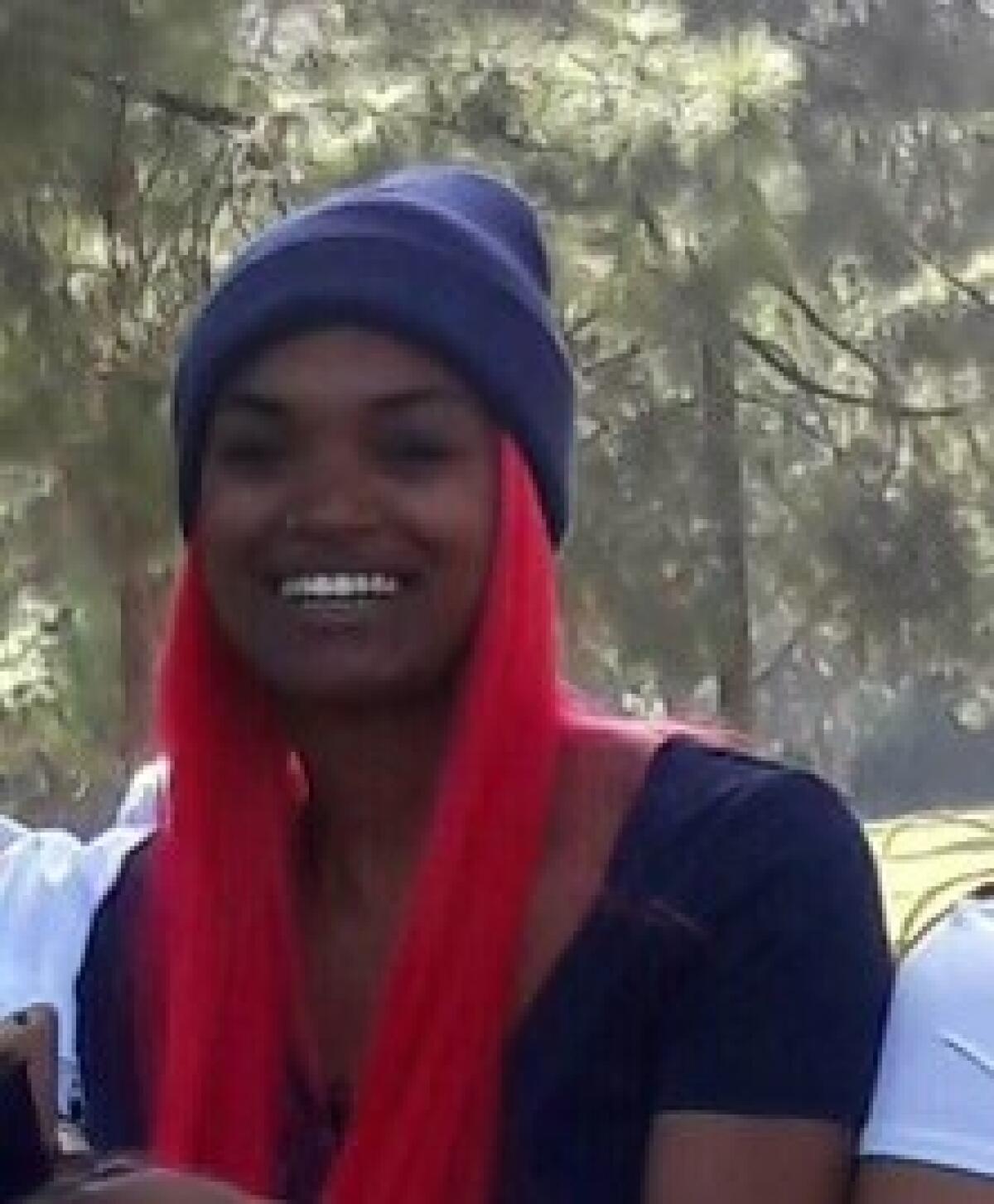 A Black woman with long pink hair and a blue beanie.