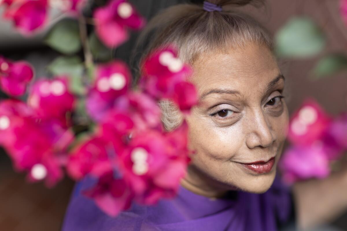 An older woman with her hair pulled back is framed by pink flowers.