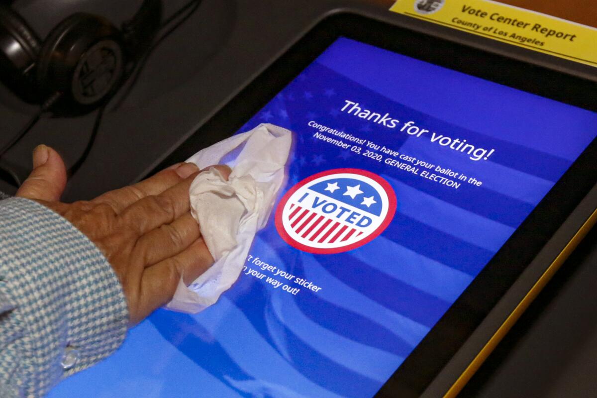 Clerk Cristina Madrid sanitizes polling booths after every use at an in-person early voting place at Azusa Women's Club.