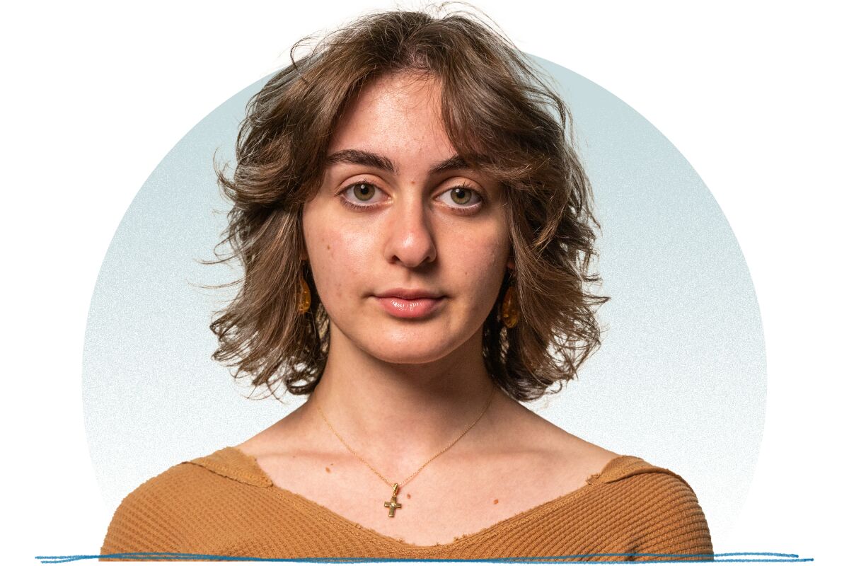 A young woman with medium brunette hair and a light brown sweater posing for a portrait.